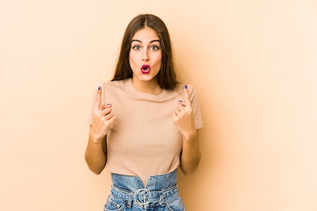 Young caucasian woman isolated en beige space pointing upside with opened mouth.