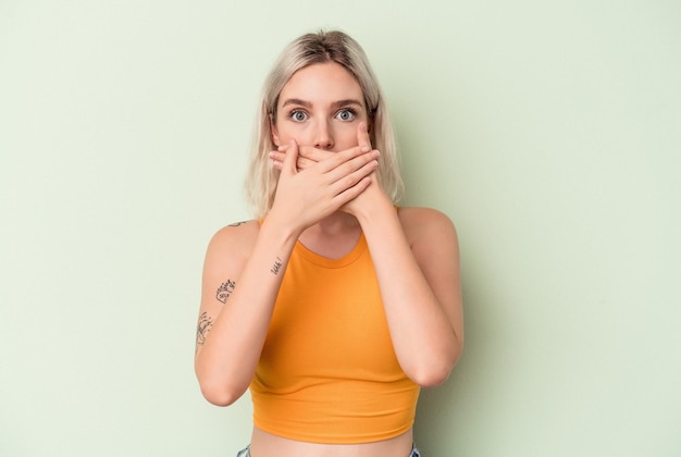 Young caucasian woman isolated on green background covering mouth with hands looking worried.