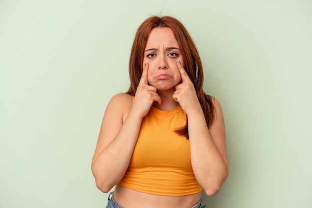 Young caucasian woman isolated on green background crying, unhappy with something, agony and confusion concept.