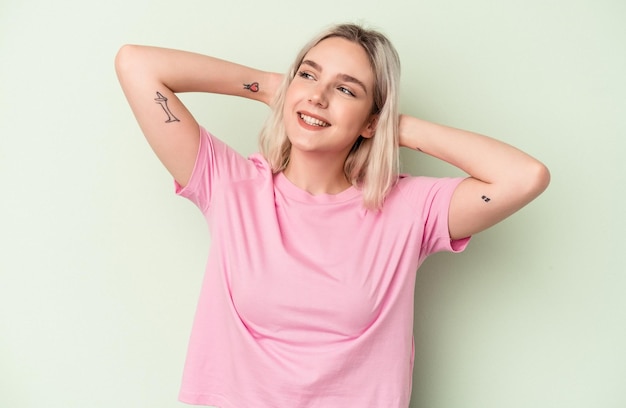 Young caucasian woman isolated on green background feeling confident, with hands behind the head.