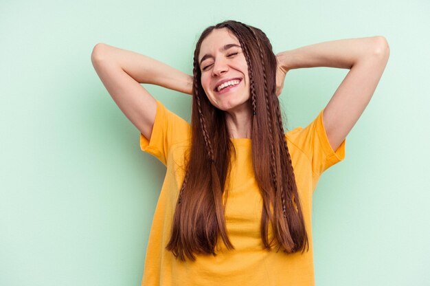 Young caucasian woman isolated on green background feeling confident with hands behind the head