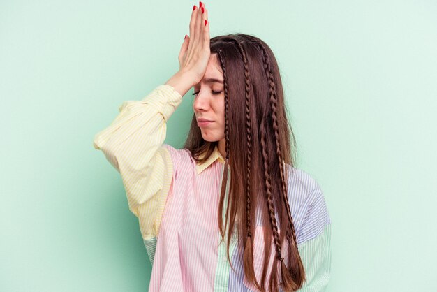 Young caucasian woman isolated on green background forgetting something, slapping forehead with palm and closing eyes.