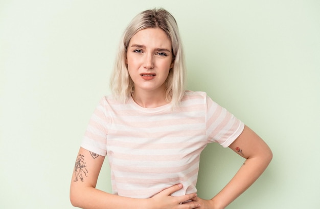 Young caucasian woman isolated on green background having a liver pain, stomach ache.