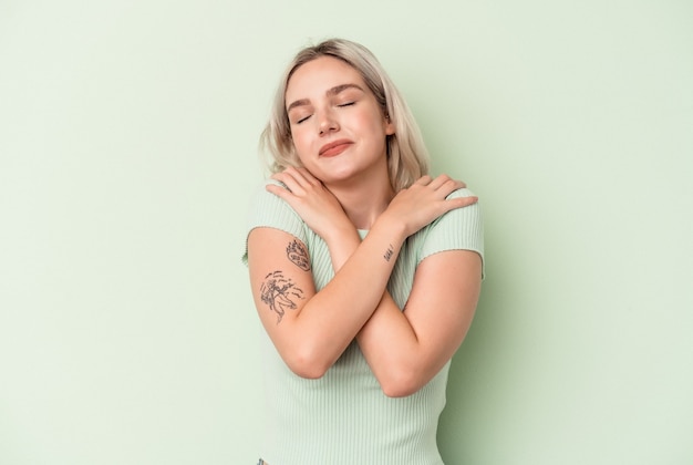 Young caucasian woman isolated on green background hugs, smiling carefree and happy.