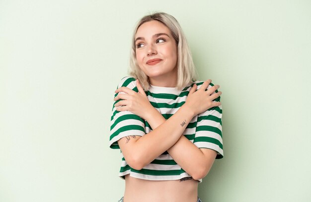Young caucasian woman isolated on green background hugs, smiling carefree and happy.