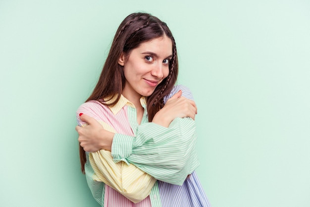 Young caucasian woman isolated on green background hugs, smiling carefree and happy.