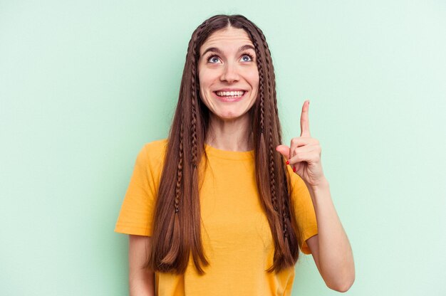 Young caucasian woman isolated on green background indicates with both fore fingers up showing a blank space.