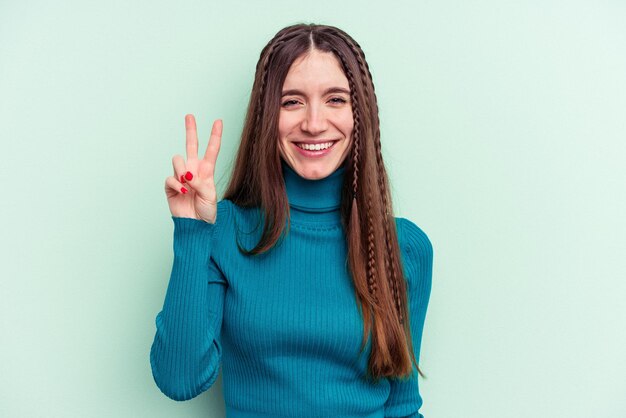 Young caucasian woman isolated on green background joyful and carefree showing a peace symbol with fingers