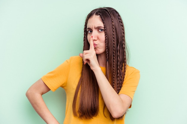 Young caucasian woman isolated on green background keeping a secret or asking for silence