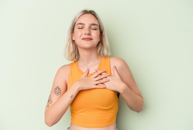 Young caucasian woman isolated on green background laughing keeping hands on heart, concept of happiness.