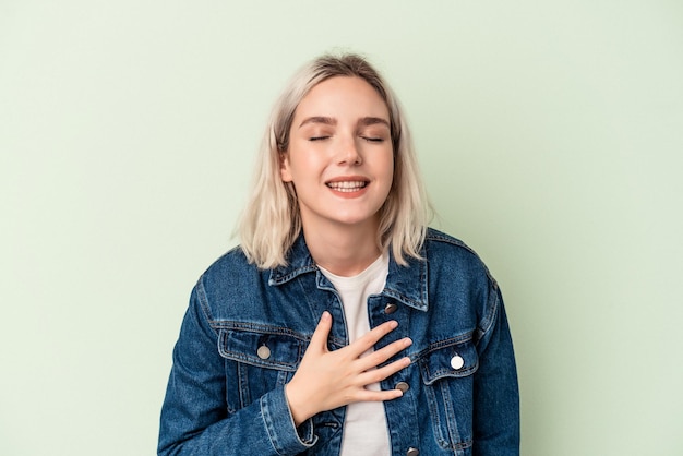 Young caucasian woman isolated on green background laughs out loudly keeping hand on chest.