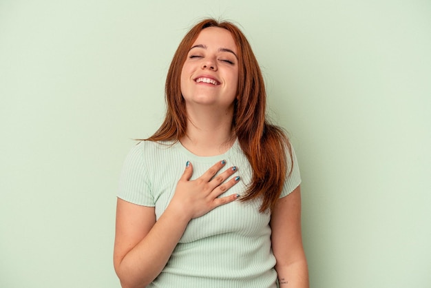 Young caucasian woman isolated on green background laughs out loudly keeping hand on chest.