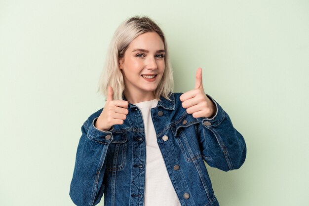 Young caucasian woman isolated on green background raising both thumbs up, smiling and confident.