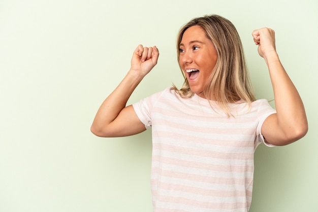 Photo young caucasian woman isolated on green background raising fist after a victory, winner concept.