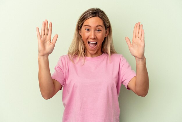 Young caucasian woman isolated on green background receiving a pleasant surprise, excited and raising hands.