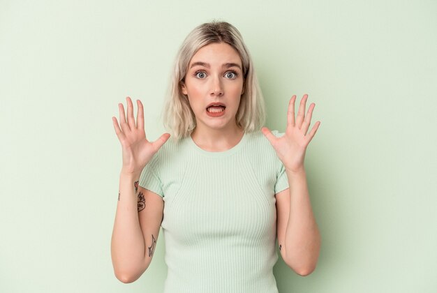 Young caucasian woman isolated on green background screaming to the sky, looking up, frustrated.