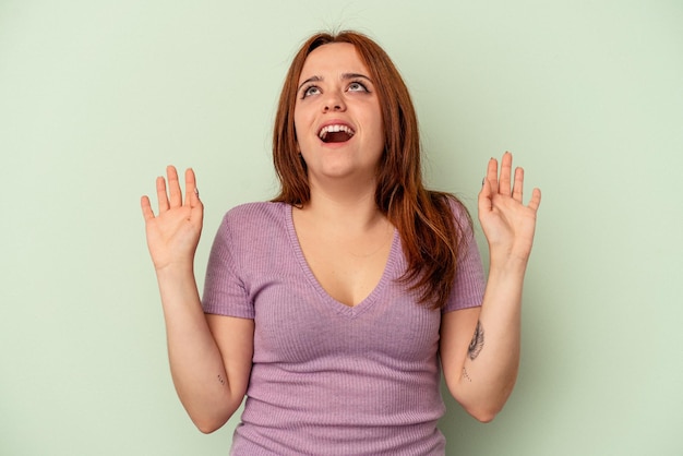 Young caucasian woman isolated on green background screaming to the sky, looking up, frustrated.