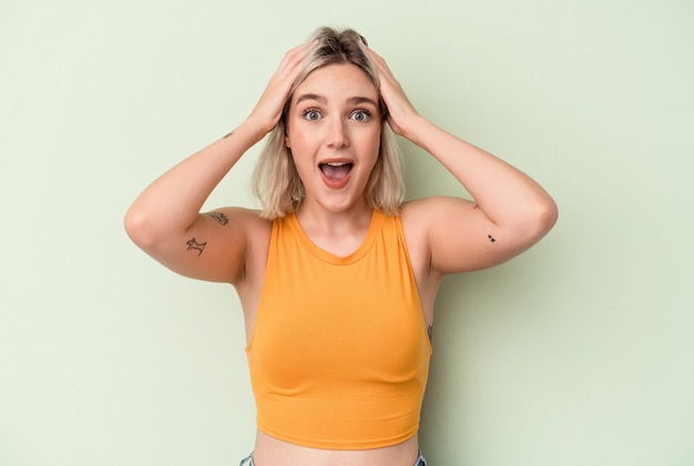 Young caucasian woman isolated on green background screaming, very excited, passionate, satisfied with something.