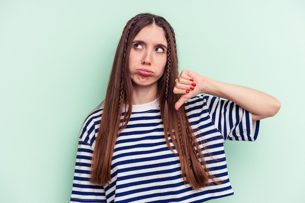 Young caucasian woman isolated on green background showing a dislike gesture, thumbs down. Disagreement concept.