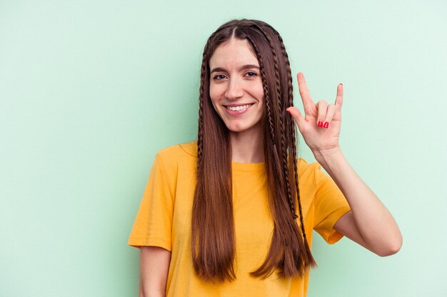 Young caucasian woman isolated on green background showing a horns gesture as a revolution concept