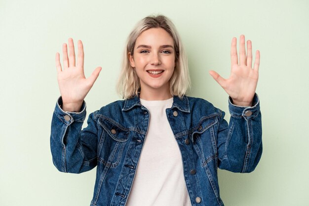 Young caucasian woman isolated on green background showing number ten with hands.