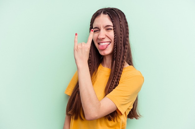 Young caucasian woman isolated on green background showing rock gesture with fingers