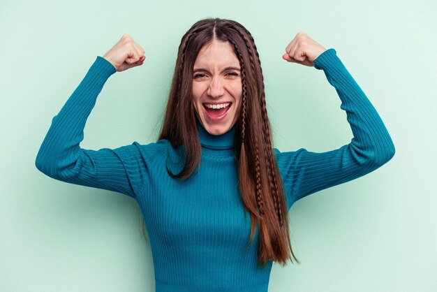 Foto giovane donna caucasica isolata su sfondo verde che mostra il gesto di forza con le braccia, simbolo del potere femminile