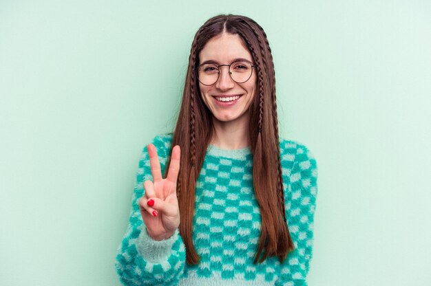 Young caucasian woman isolated on green background showing
victory sign and smiling broadly.