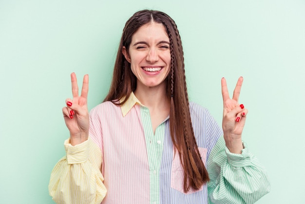 Young caucasian woman isolated on green background showing
victory sign and smiling broadly