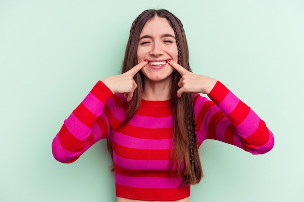 Young caucasian woman isolated on green background smiles, pointing fingers at mouth.