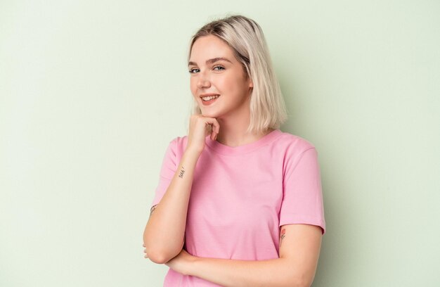 Young caucasian woman isolated on green background smiling happy and confident, touching chin with hand.