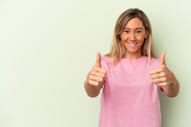 Young caucasian woman isolated on green background smiling and raising thumb up