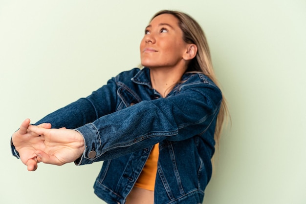 Young caucasian woman isolated on green background stretching arms, relaxed position.