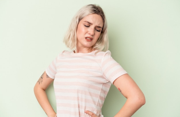 Young caucasian woman isolated on green background suffering a back pain.