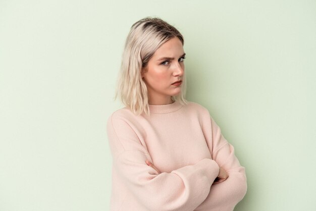 Young caucasian woman isolated on green background suspicious, uncertain, examining you.