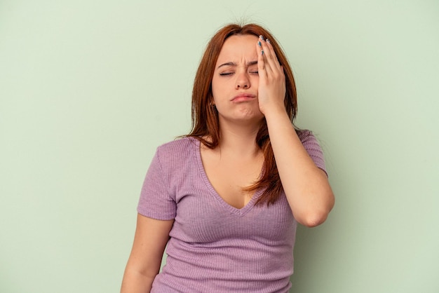 Young caucasian woman isolated on green background tired and very sleepy keeping hand on head.