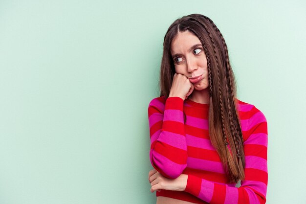 Young caucasian woman isolated on green background who feels sad and pensive, looking at copy space.