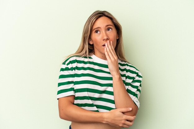 young caucasian woman isolated on green background yawning showing a tired gesture covering mouth with hand.