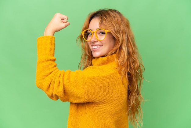 Young caucasian woman isolated on green screen chroma key background With glasses and celebrating a victory