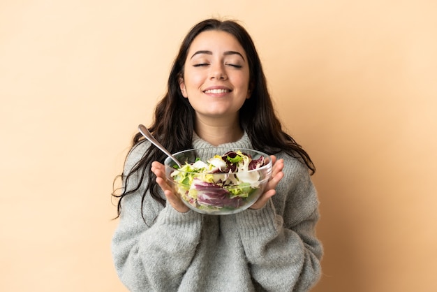 Young caucasian woman isolated  holding a bowl of salad with happy expression