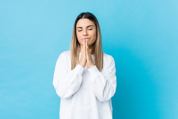 Young caucasian woman isolated holding hands in pray near mouth, feels confident.