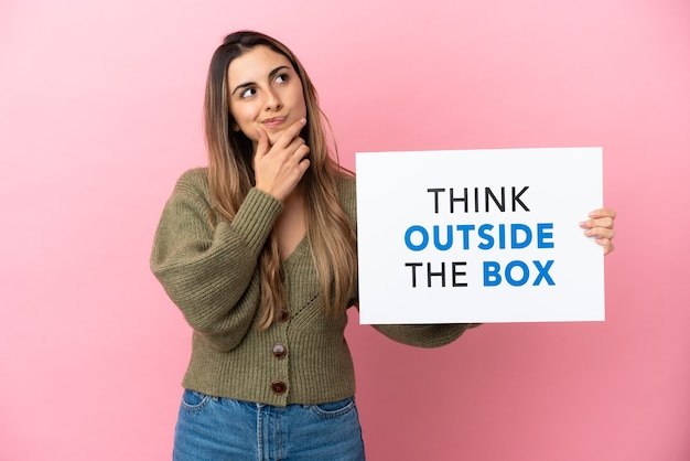Young caucasian woman isolated holding a placard with text Think Outside The Box and thinking