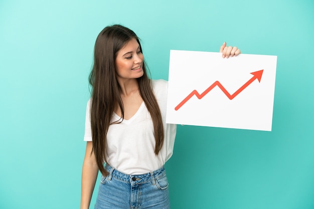 Photo young caucasian woman isolated holding a sign with a growing statistics arrow