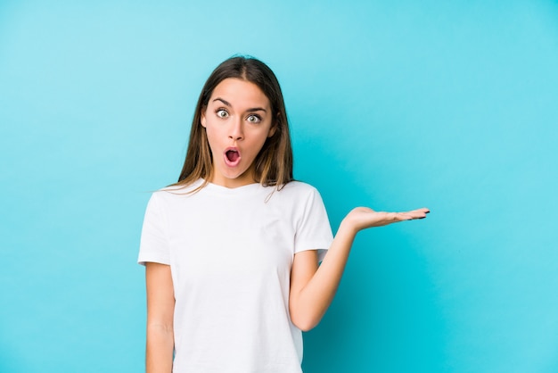 Young caucasian woman  isolated impressed holding copy space on palm.