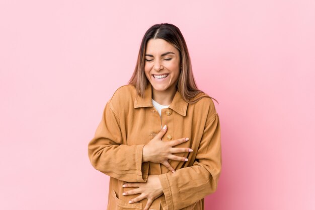 Young caucasian woman isolated laughs happily and has fun keeping hands on stomach.