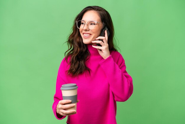 Фото Молодая белая женщина, изолированная на изолированном фоне, держит кофе и мобильный телефон.