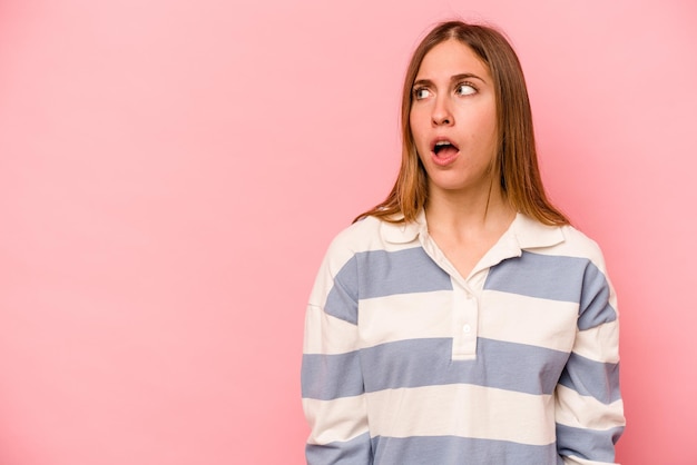 Young caucasian woman isolated on pink background being shocked because of something she has seen