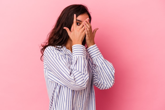 Young caucasian woman isolated on pink background blink through fingers frightened and nervous.