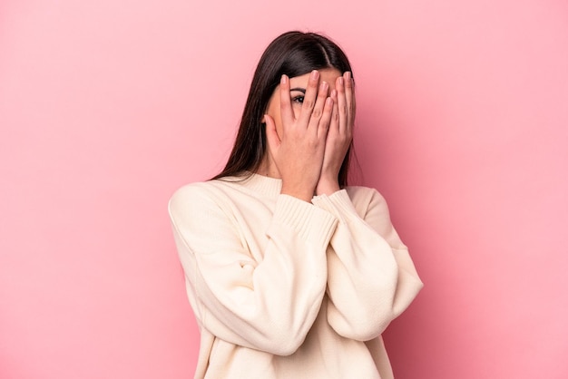 Young caucasian woman isolated on pink background blink through fingers frightened and nervous