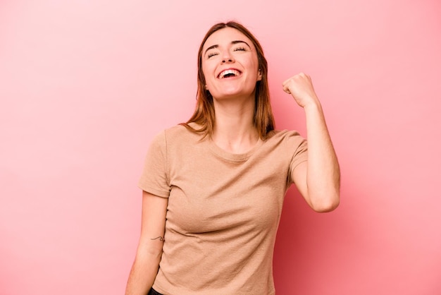 勝利の情熱と熱意の幸せな表現を祝うピンクの背景に分離された若い白人女性